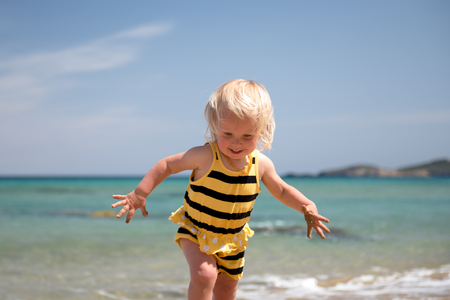 Cute baby girl having fun on the beach playing with wavesの写真素材