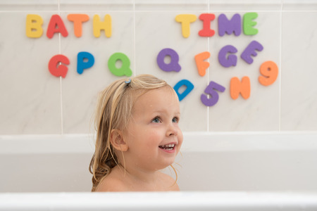 Smiling little girl in bathroom with colorful foam letters and numbers in background. Water fun for kids.の写真素材