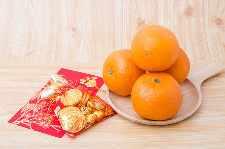 Chinese New Year - Mandarin orange, gold sycee (Foreign text means wealth) and red packet (Foreign text means spring season) on white painted wood tableの写真素材