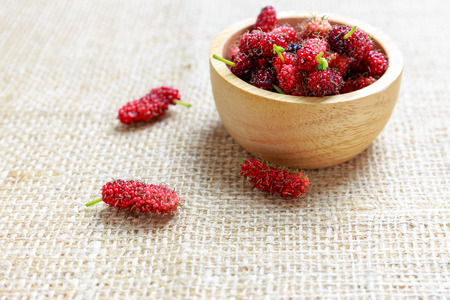 Red mulberry in wooden bowl and on cloth floor, healthy fruitの写真素材