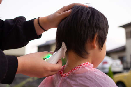 Mother cutting her child's hair with clippers in the gardenの写真素材