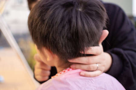 Mother cutting her child's hair with clippers in the garden
