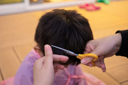 Mother cutting child's hair with scissors in the gardenの写真素材