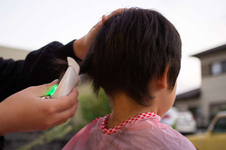 Mother cutting her child's hair with clippers in the gardenの写真素材