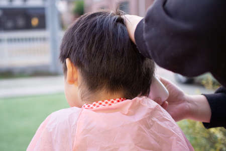 Mother cutting her child's hair with clippers in the gardenの写真素材