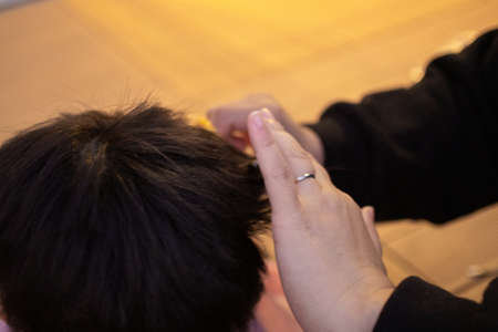 Mother cutting child's hair with scissors in the garden