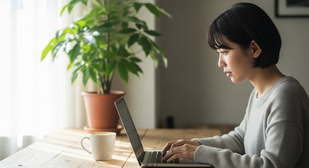 A Japanese woman works in a home cafÃ© nook with a logo-free mug and plants. Soft natural light expresses home-working calmly.の素材