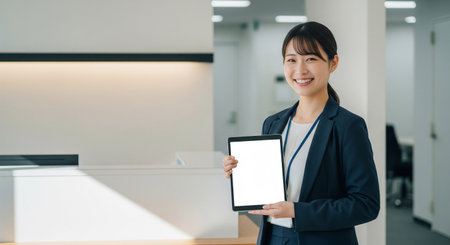 A young Japanese employee holds a blank tablet near office receptionâclean and ideal for recruiting and company pages.の素材