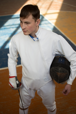 fencer in the sports room in a mask and with a sword in a hand. the fencer prepares for...