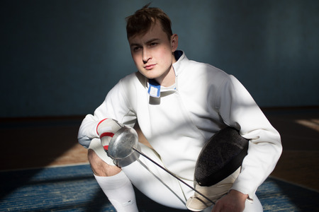 fencer in the sports room in a mask and with a sword in a hand. the fencer prepares for competitions. fencing coach. fencing sport motivation. mask and swordの写真素材