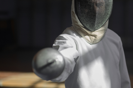 fencer in the sports room in a mask and with a sword in a hand. the fencer prepares for competitions. fencing coach. fencing sport motivation. mask and swordの写真素材