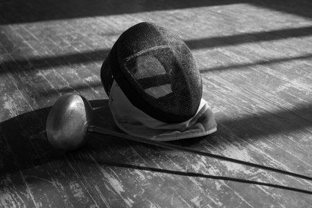 fencer in the sports room in a mask and with a sword in a hand. the fencer prepares for...