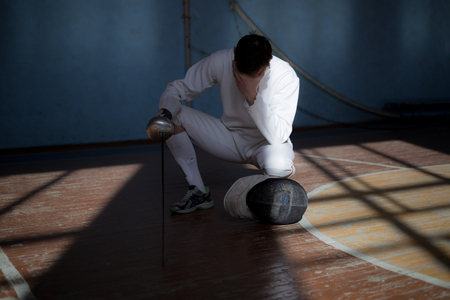 fencer in the sports room in a mask and with a sword in a hand. the fencer prepares for...