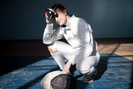fencer in the sports room in a mask and with a sword in a hand. the fencer prepares for...