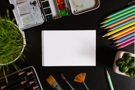 Flat lay watercolor workplace with color pencils, paint brushes with white paper and copy space