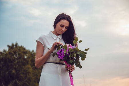 Outdoors portrait of a gorgeous young brunette woman holding lavender flowers.の写真素材