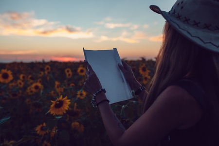 Girl in a cowboy hat in a sunflower field with a map looking for the path. Sunsetの写真素材
