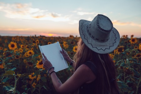 Girl in a cowboy hat in a sunflower field with a map looking for the path. Sunsetの写真素材