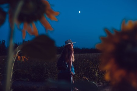 She lost in the sunflower field sits on a suitcase. Waiting for help. Night.の写真素材