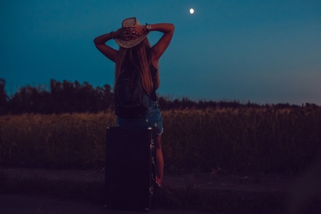 She lost in the sunflower field sits on a suitcase. Waiting for help. Night.の写真素材