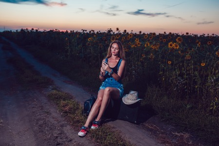 Girl sitting on a suitcase in a sunflower field. Sunset.の写真素材