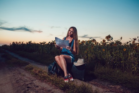 Girl sitting on a suitcase in a sunflower field. Sunset.の写真素材