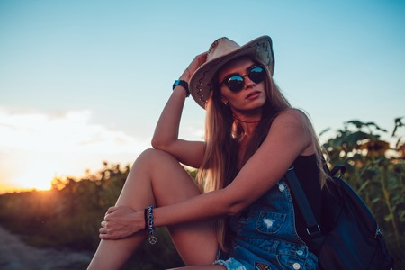 Girl in cowboy hat sitting on a suitcase in a sunflower field. Sunset.の写真素材