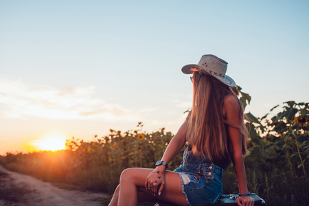 Girl in cowboy hat sitting on a suitcase in a sunflower field. Sunset.の写真素材