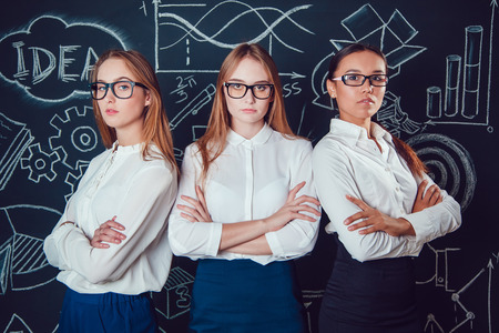 Two Europeans and Asian business women with glasses standing on a dark background patternの写真素材