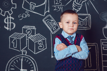 Little boy as businessman or teacher standing with her hands folded on a dark background with patternの写真素材
