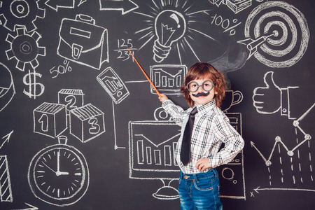 Little boy as businessman or teacher with mustache and glasses standing on a dark background pattern. Wearing shirt and tieの写真素材