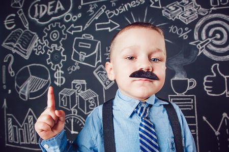 Little boy as businessman or teacher with mustache and glasses standing on dark background pattern. Wearing shirt, tie. Lifting a finger upの写真素材