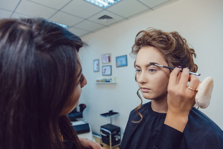 make up artist doing professional make up of young woman