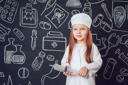 Happy little girl as a doctor in glasses holding syringe on dark background with patternの写真素材