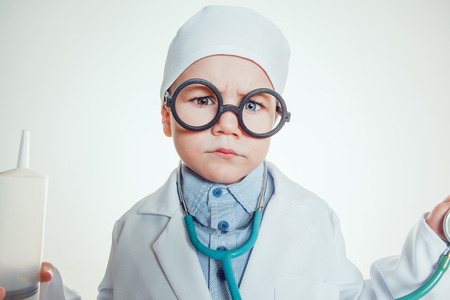 Happy little boy in doctor costum with glasses holding syringe and sthetoscope on white background.の写真素材