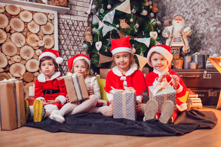 Children dressed as Santa Claus sitting with gifts in on Christmas decoration. New Year.の写真素材