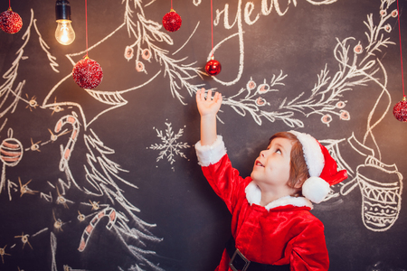 Little boy dressed as Santa Claus standing on dark background with Christmas pattern. New Year.の写真素材