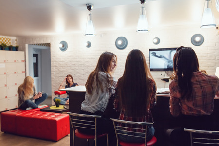 Beautiful girls sitting at the bar in Hostel, watching tv and talk.の写真素材