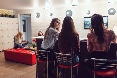 Beautiful girls sitting at the bar in Hostel, watching tv and talk.の写真素材