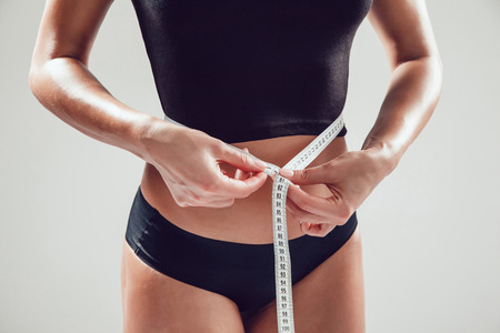 Athletic slim woman measuring her waist by measure tape on white backgroundの写真素材