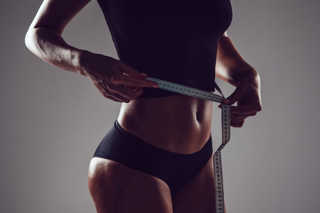 Athletic slim woman measuring her waist by measure tape on grey backgroundの写真素材