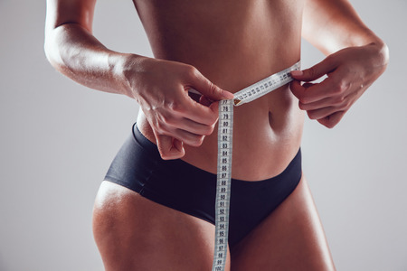 Athletic slim woman measuring her waist by measure tape on white backgroundの写真素材