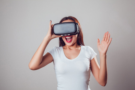 Attractive and happy woman using virtual reality goggles on grey background. VR headset.の写真素材