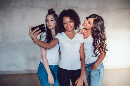 Three pretty girls grimace and make selfie on grey background.の写真素材