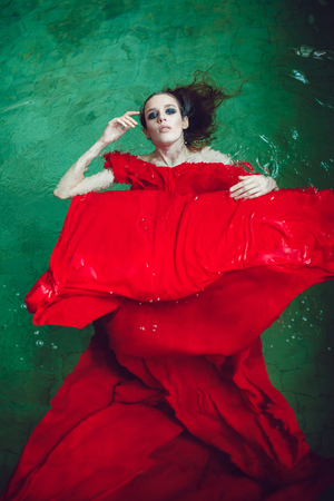 Fashion brunette woman with beautiful professional make up floating in a pool of red cloth.の写真素材