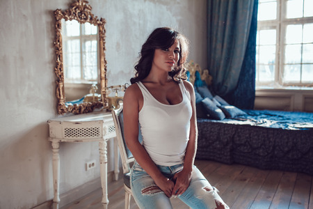 Beautiful young woman dressed white blank tank-top sitting in the old style room. Mock-up.の写真素材