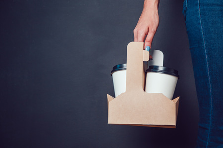 Woman holding a blank takeaway coffee cups on black background. Mock up.の写真素材