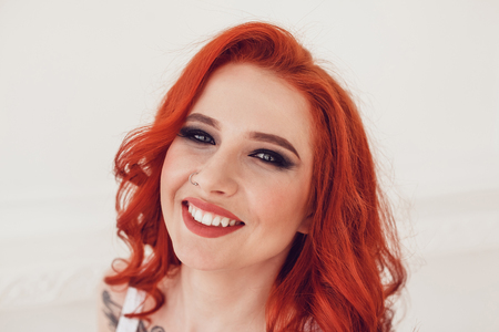 Portrait of a beautiful sexy girl with red hair and a tattoo. Woman with make-up and curls.の写真素材