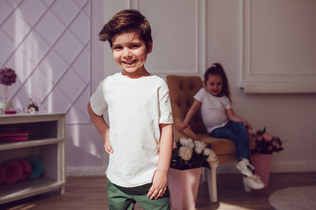 Two children in blank white t-shirts. The boy is standing and girl sitting behind him. Mock up.の写真素材