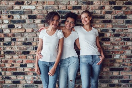 Three attractive girls in white T-shirts are standing on a brick wall background.の写真素材